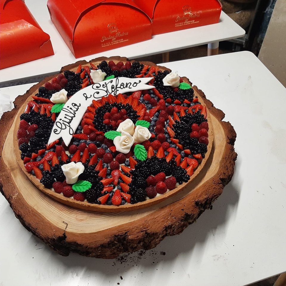 Crostata personalizzata ai frutti di bosco con rose bianche su un vassoio di legno