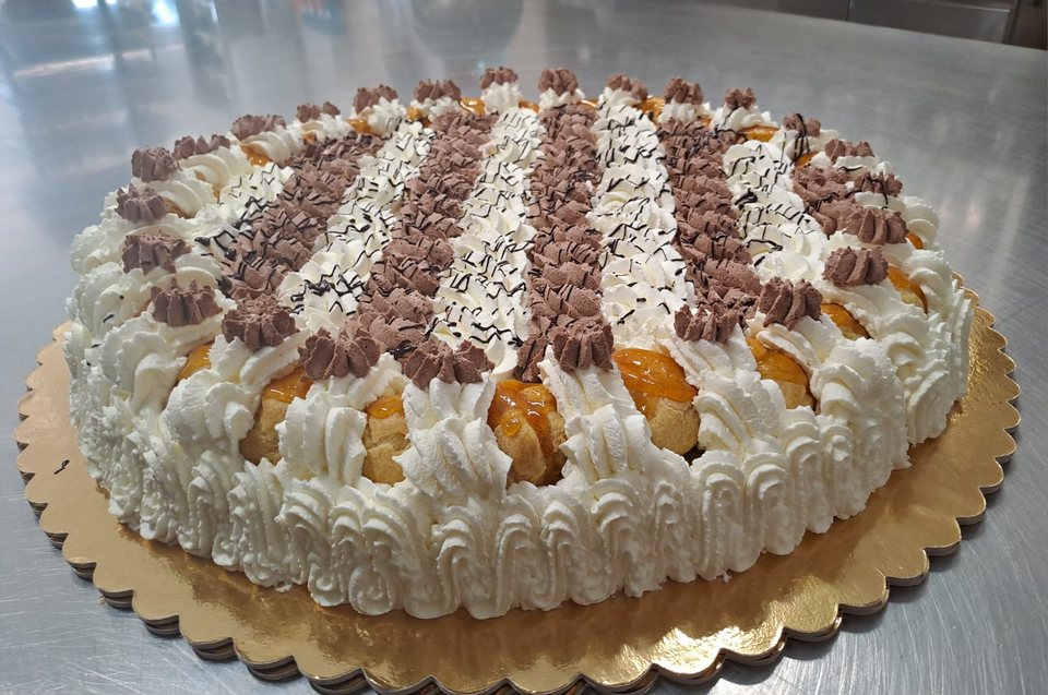 Cake with glazed choux buns, swirls of cream and chocolate decorations